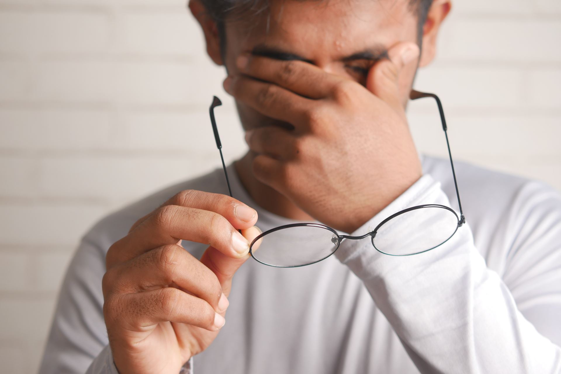 a man holding his left hand over his face with his glasses in his right hand