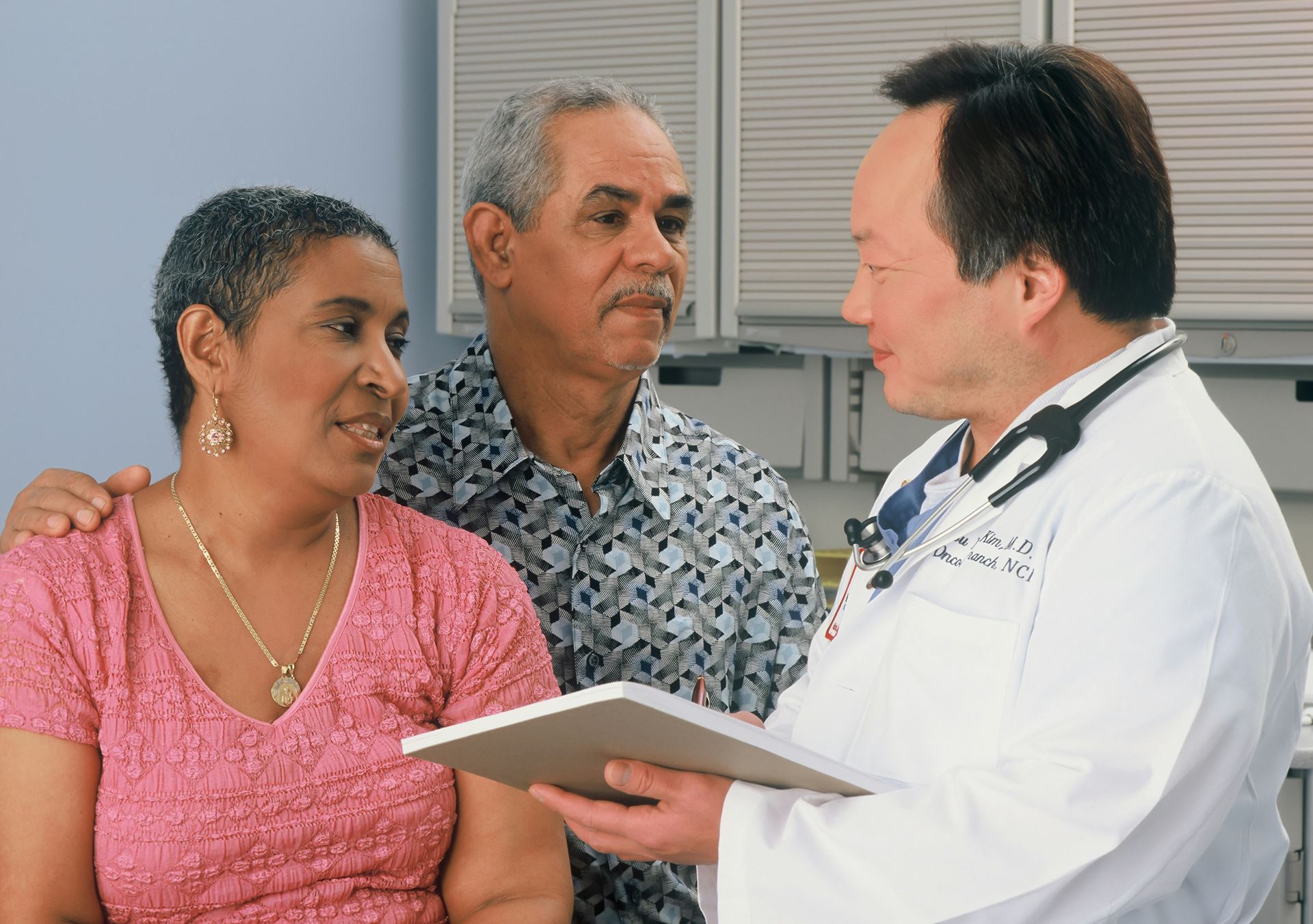 a man and a woman speaking with a doctor.  The doctor has a stethoscope handing around his neck